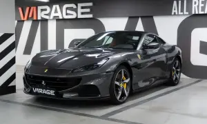 Szary Ferrari Portofino z żółtymi zaciskami hamulcowymi stoi w garażu z napisem "VIRAGE" na tablicy rejestracyjnej.