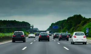 Samochody jadące drogą szybkiego ruchu w pochmurny dzień. Widać kilka pasów ruchu i zielone drzewa po bokach.
