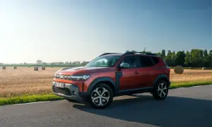 Nowa Dacia Duster w kolorze rudym, zaparkowana na poboczu drogi, z polem słomy w tle.