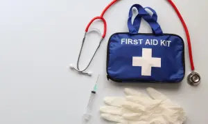 Niebieska apteczka samochodowa z białym krzyżem, stetoskop, strzykawka i rękawiczki. Czy apteczka jest obowiązkowa w samochodzie? Zdecydowanie tak!