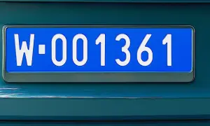 Niebieskie tablice rejestracyjne z numerem W-001361 na ciemnozielonym samochodzie.