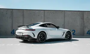 Biały Mercedes GT 63 AMG z czarnym spoilerem i felgami, zaparkowany pod betonową ścianą z niebieskimi cyframi.