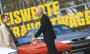 Dwóch mężczyzn ogląda sportowe auta. Jeden wskazuje na czerwony samochód, drugi stoi obok.