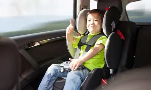 Uśmiechnięty chłopiec w foteliku samochodowym pokazuje kciuk w górę. Bezpieczna podróż to podstawa, nawet dla dziecka bez fotelika.