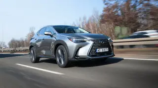 Srebrny Lexus NX 450h+ pędzi autostradą, otoczony jesienną scenerią.