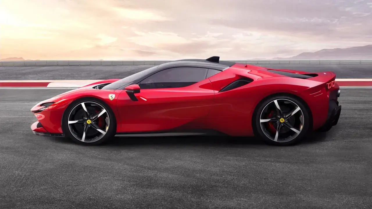 Czerwone Ferrari SF90 na torze wyścigowym, z czarnym dachem i felgami. Słońce zachodzi za górami.