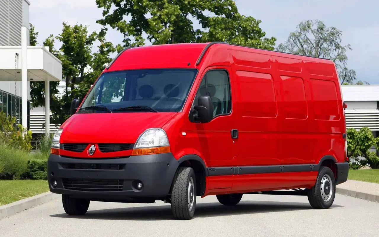 Czerwony Renault Master 2, gotowy do pracy, stoi na tle zieleni i nowoczesnego budynku.