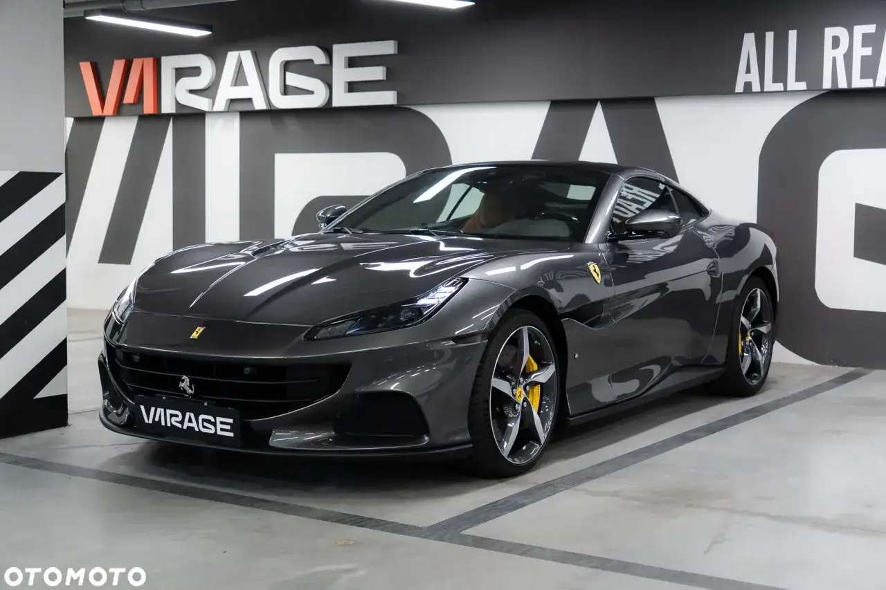 Szary Ferrari Portofino z żółtymi zaciskami hamulcowymi stoi w garażu z napisem "VIRAGE" na tablicy rejestracyjnej.