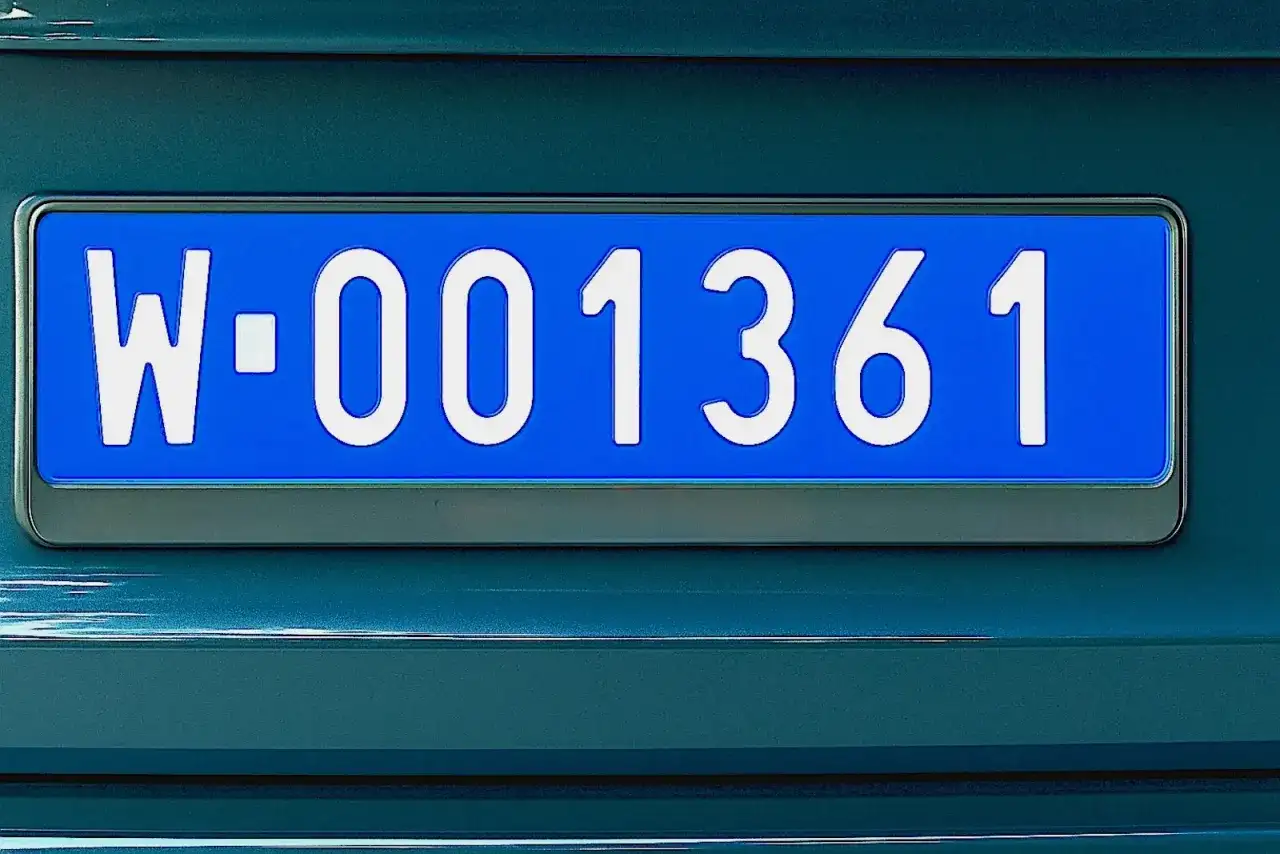 Niebieskie tablice rejestracyjne z numerem W-001361 na ciemnozielonym samochodzie.