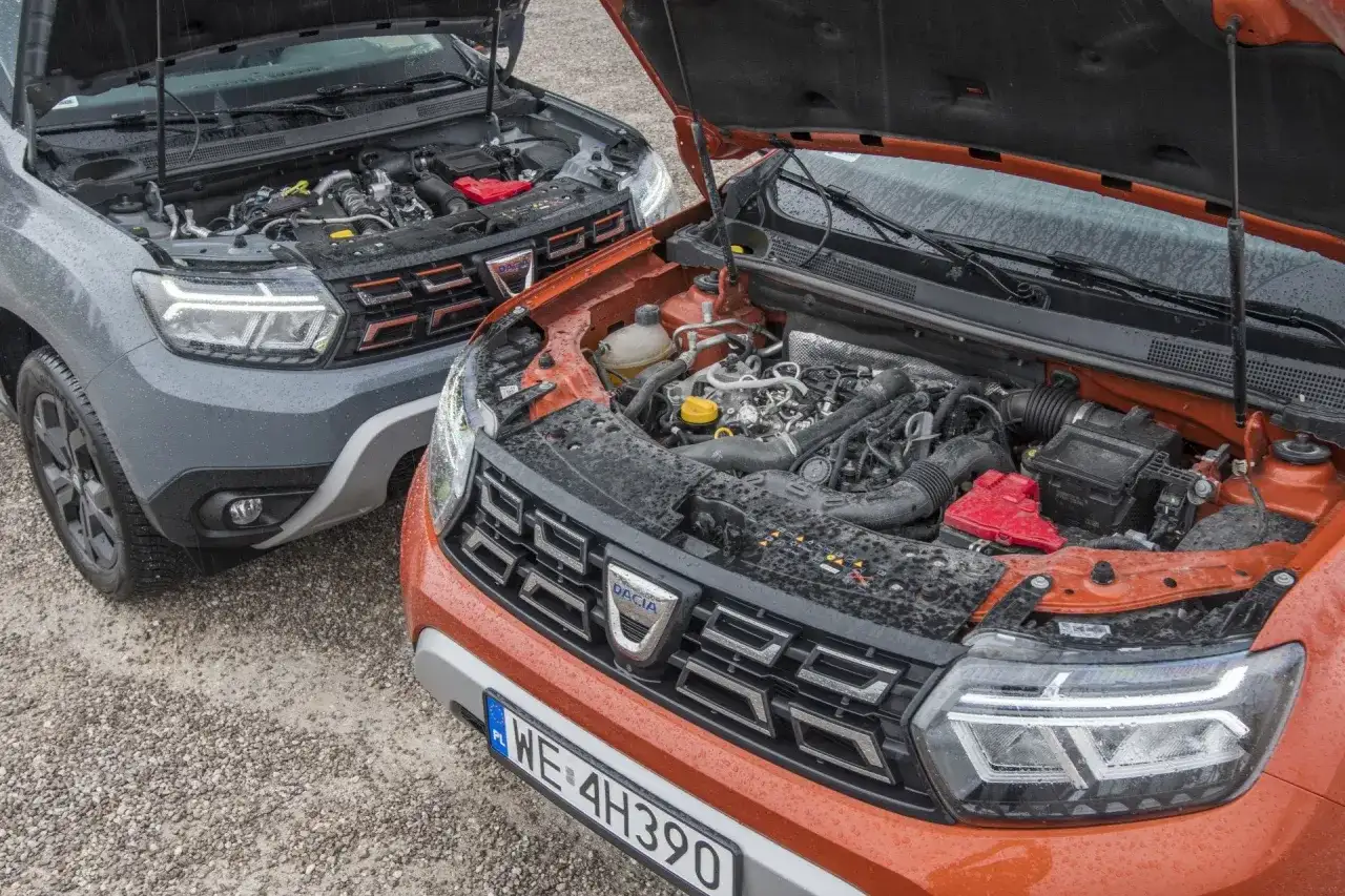 Dwa silniki Dacia Duster, szary i pomarańczowy, z otwartymi maskami. Który wybierzesz: diesel czy benzyna?