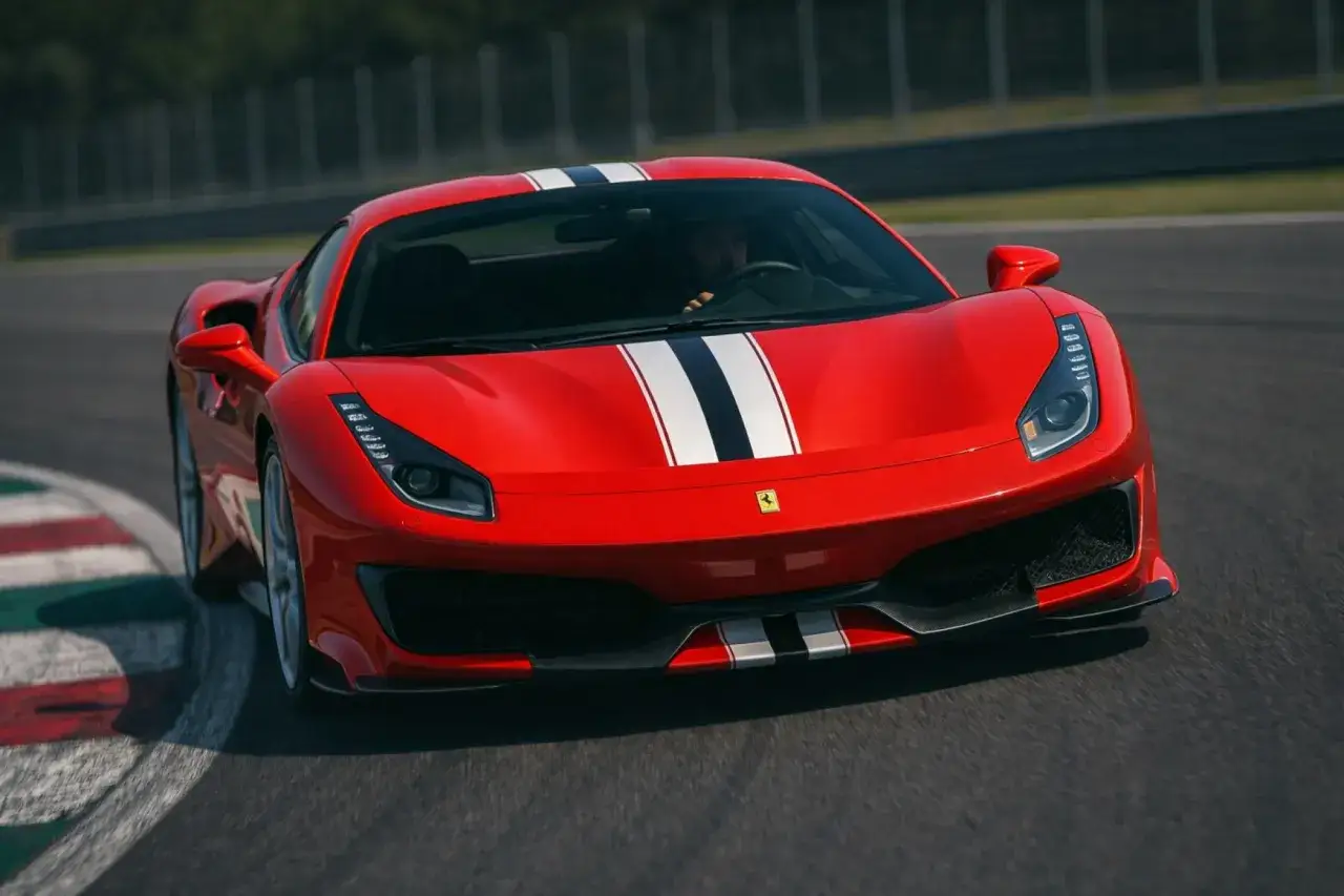Czerwone Ferrari 488 Pista z białymi i czarnymi pasami pędzi po torze wyścigowym, pokonując zakręt.