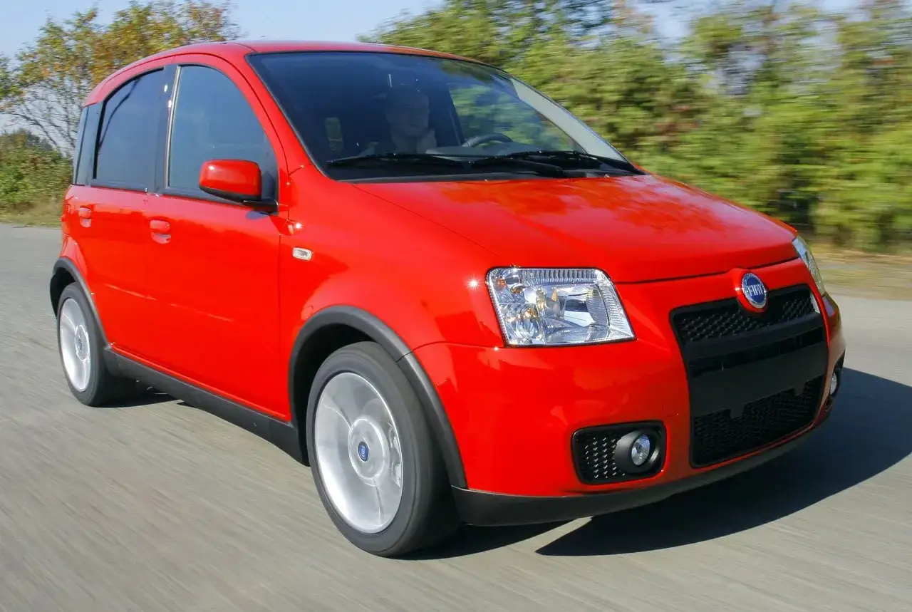 Czerwony Fiat Panda, kompaktowy kei car, pędzi po drodze, otoczony zielenią.