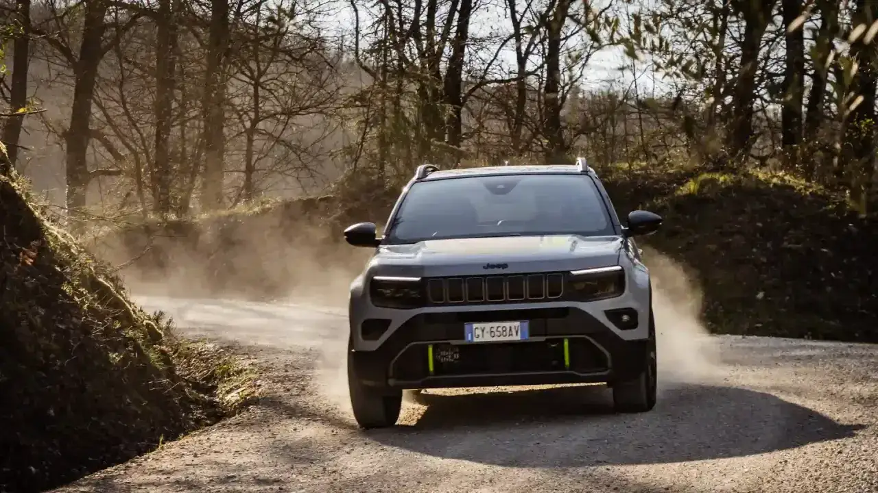 Szary Jeep Avenger 4xe pokonuje zakurzoną, leśną drogę, unosząc tumany pyłu.