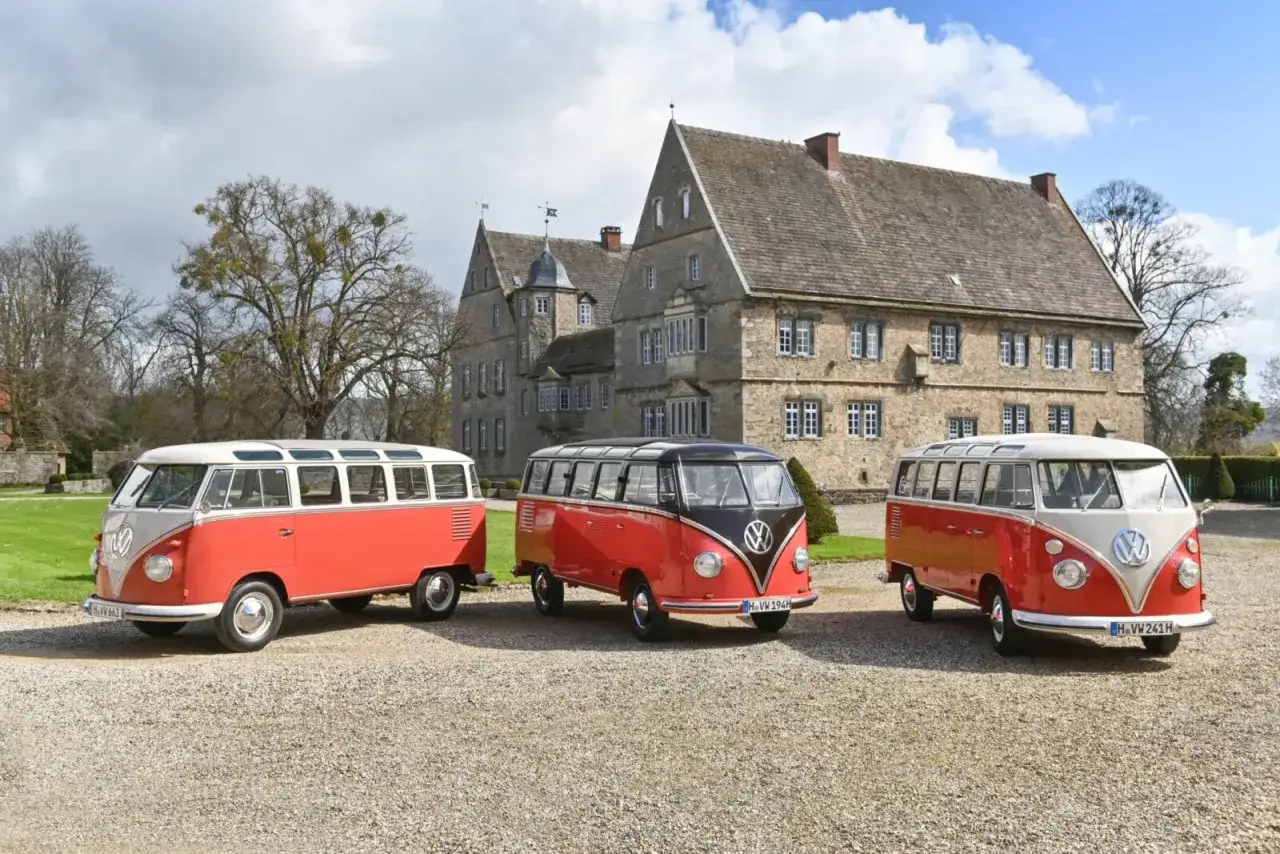 Trzy klasyczne VW T1 w kolorach czerwonym i kremowym stoją przed kamiennym pałacem.