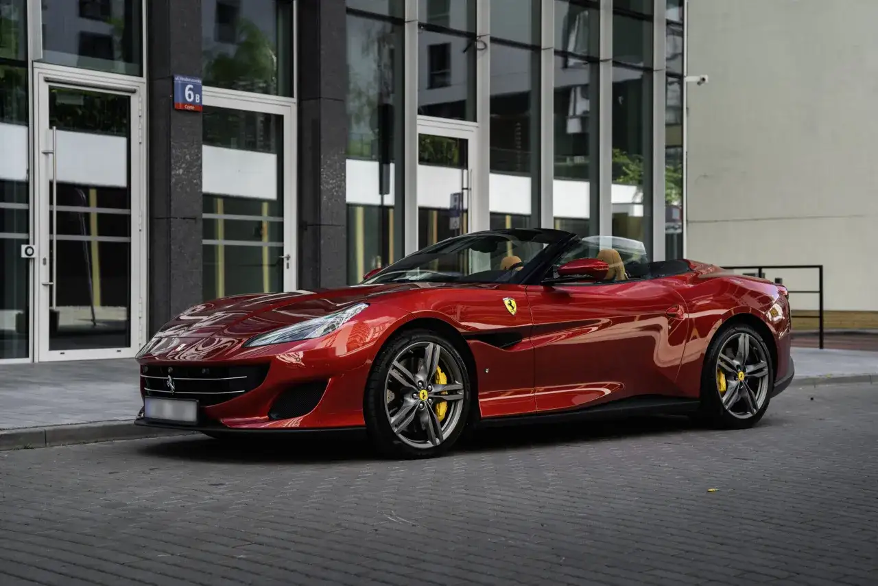 Lśniące czerwone Ferrari Portofino z beżowym wnętrzem stoi przed nowoczesnym budynkiem.