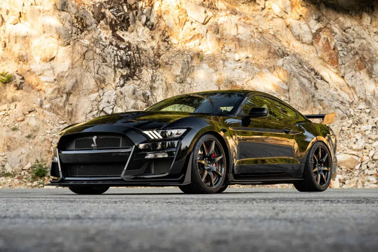 Czarny Shelby GT500 z potężnym spojlerem na tle skalistej ściany.