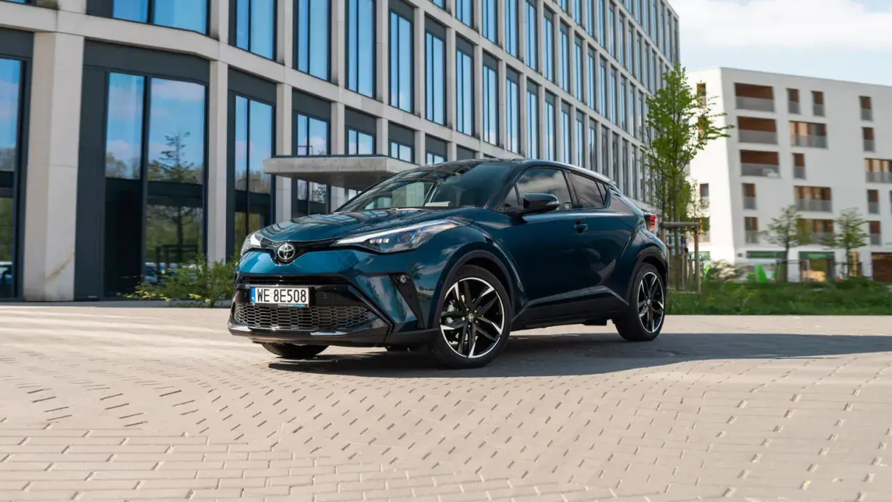 Nowoczesna, ciemnozielona Toyota C-HR hybrid zaparkowana przed biurowcem.