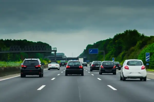 Samochody jadące drogą szybkiego ruchu w pochmurny dzień. Widać kilka pasów ruchu i zielone drzewa po bokach.