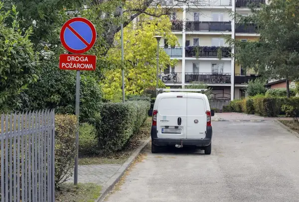 Biały Fiat parked on a fire lane. Sign "Droga pożarowa" and prohibition sign warn about potential mandat za parkowanie na zakazie.