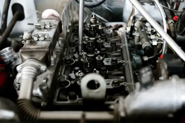 Mechanik naprawia silnik, by zapobiec spalaniu stukowemu. Widoczne zawory, wtryskiwacze i elementy układu paliwowego.
