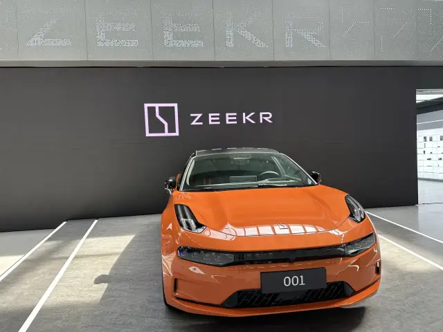 Pomarańczowy samochód marki Zeekr 001 na tle logo.